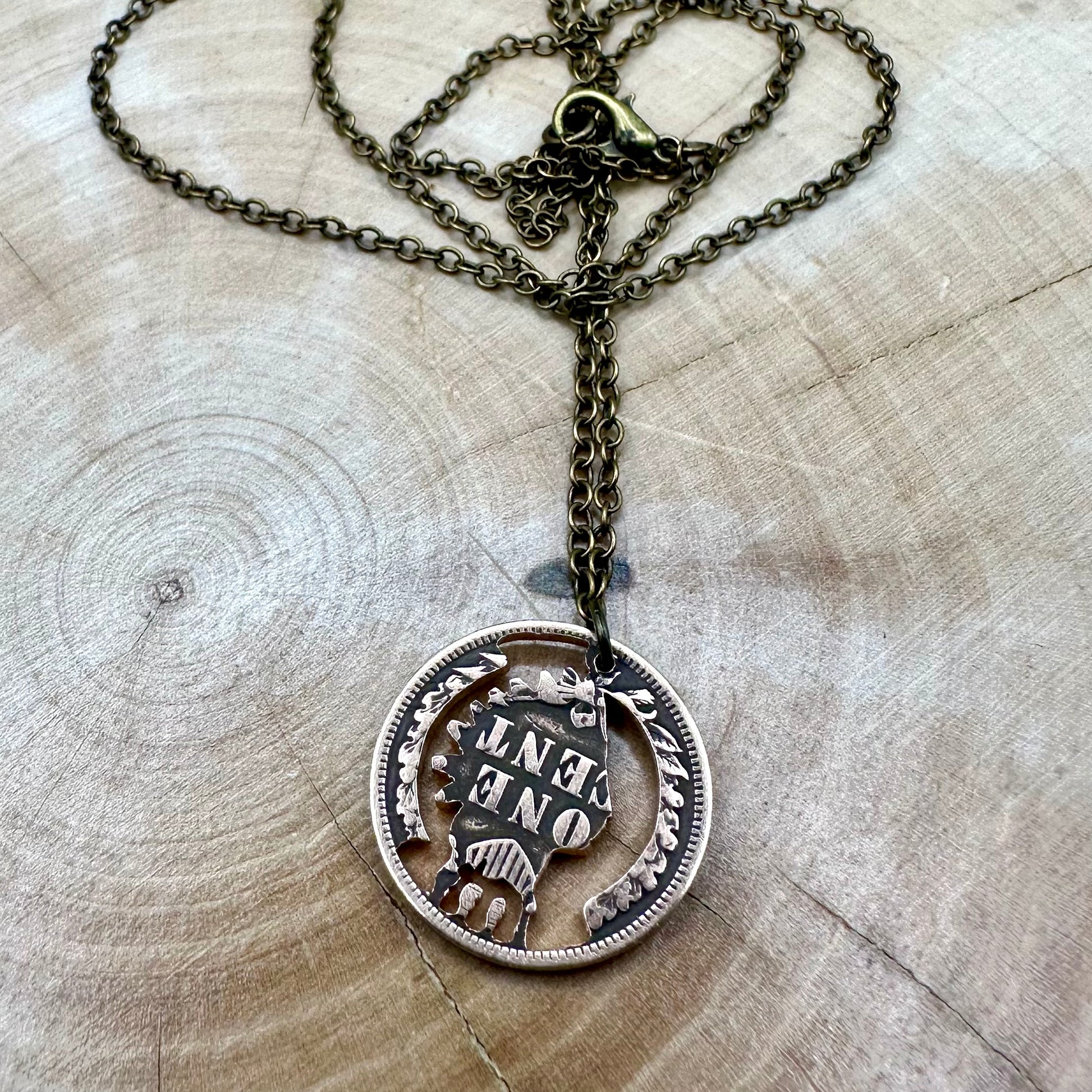 U.S. Indian Head Penny Hand Cut Coin Necklace back with bronze chain on light a wood background. - Mountainstruck Coin Jewelry