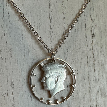 U.S. JFK Half Dollar Hand Cut Silver Coin Necklace with stainless chain on a light wood background. - Mountainstruck Coin Jewelry