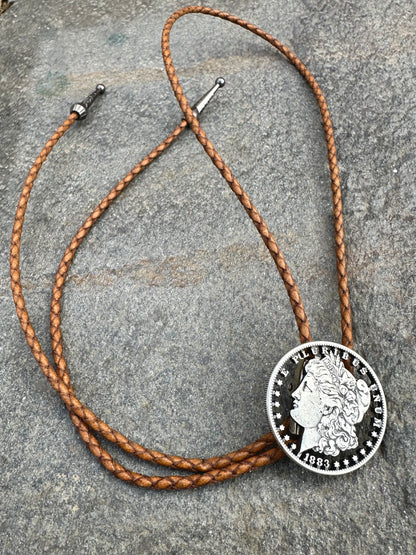 U.S. Morgan Hand Cut Silver Dollar Coin Bolo Tie (front) on a grey rock surface. - Mountainstruck Coin Jewelry