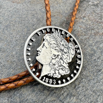 U.S. Morgan Hand Cut Silver Dollar Coin Bolo Tie (front) on a grey rock surface. - Mountainstruck Coin Jewelry