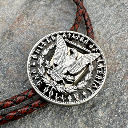 U.S. Morgan Hand Cut Silver Dollar Coin Bolo Tie (reverse) on a grey rock surface. - Mountainstruck Coin Jewelry