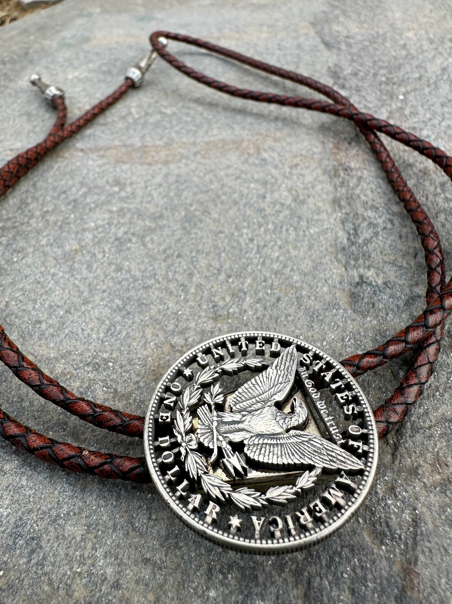 U.S. Morgan Hand Cut Silver Dollar Coin Bolo Tie (reverse) on a grey rock surface. - Mountainstruck Coin Jewelry