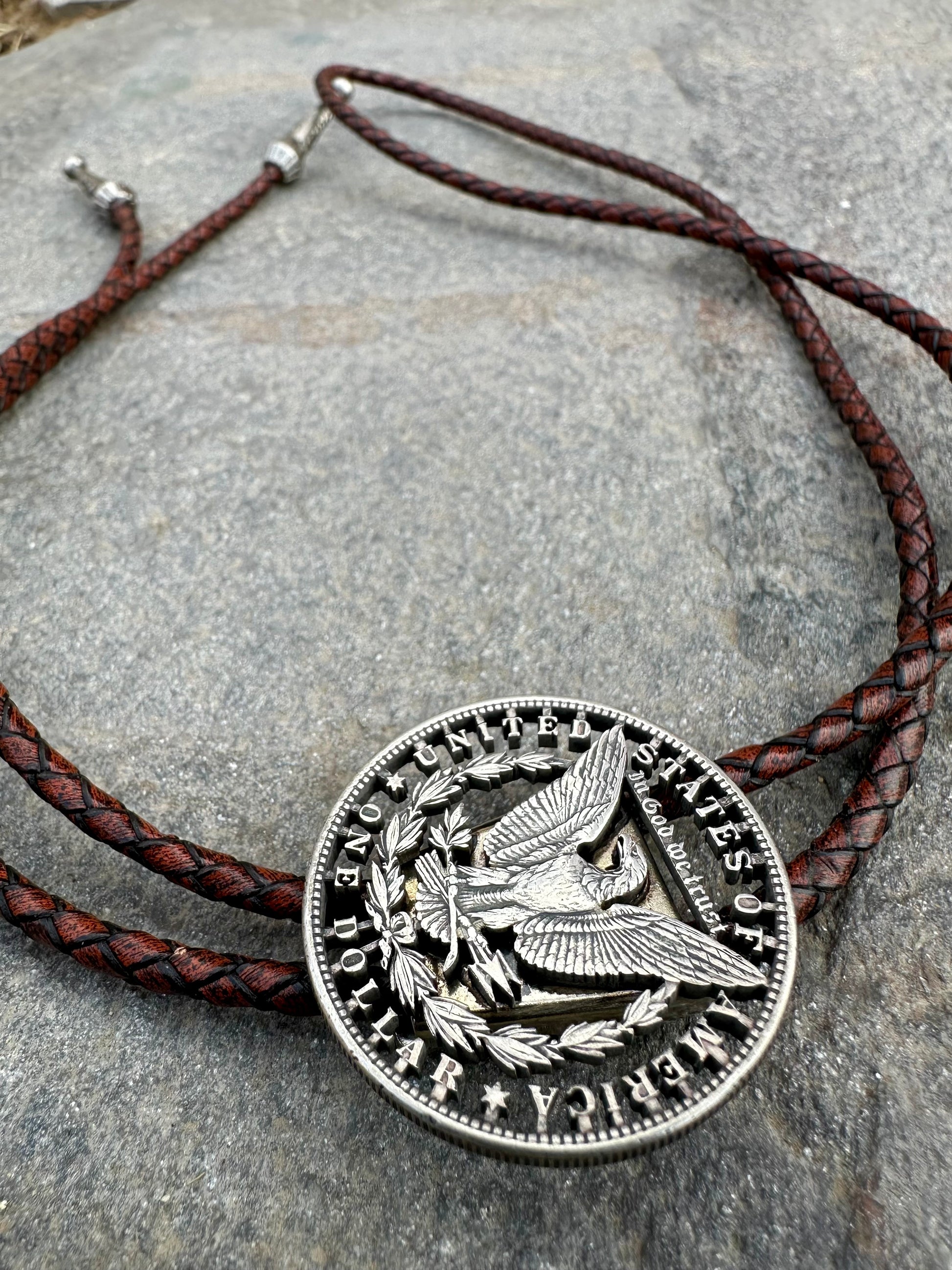 U.S. Morgan Hand Cut Silver Dollar Coin Bolo Tie (reverse) on a grey rock surface. - Mountainstruck Coin Jewelry