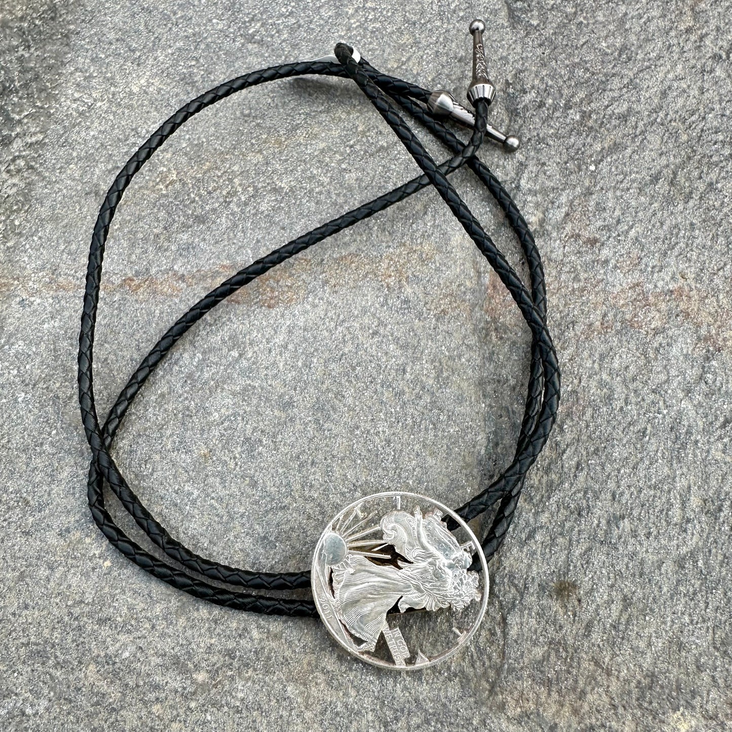 U.S. Silver Eagle Hand Cut Coin Bolo Tie on a grey rock surface. - Mountainstruck Coin Jewelry