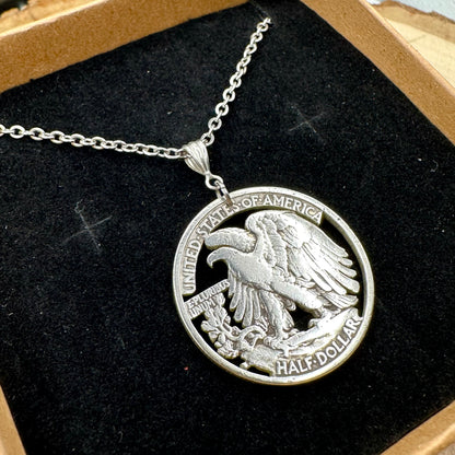 U.S. Walking Liberty Silver Hand Cut Coin Necklace (Eagle) with a stainless chain in a brown kraft box on a black velvet background on a light wood round. - Mountainstruck Coin Jewelry