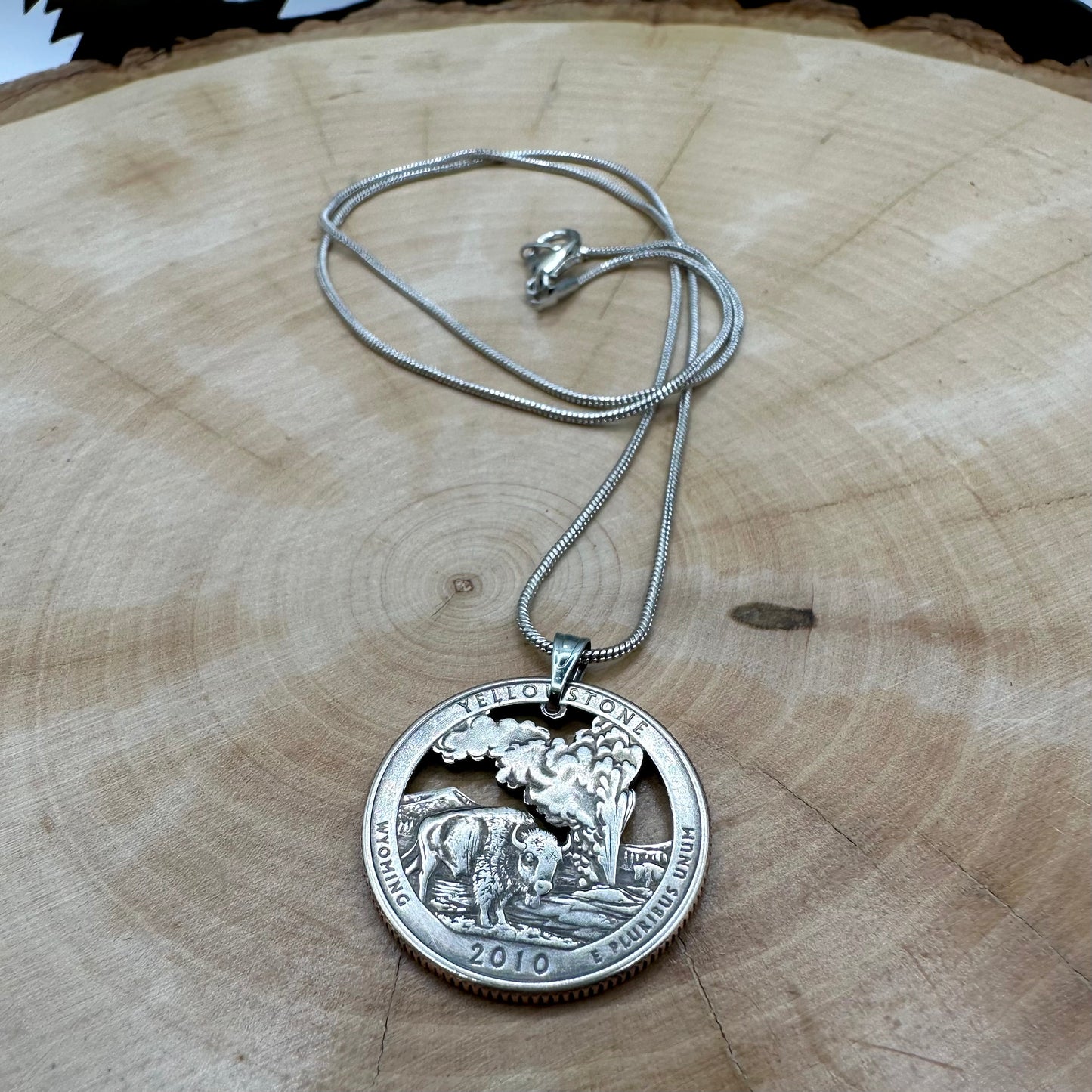 U.S. Yellowstone National Park Quarter Hand Cut Coin Necklace with snake chain on a light wood background. - Mountainstruck Coin Jewelry