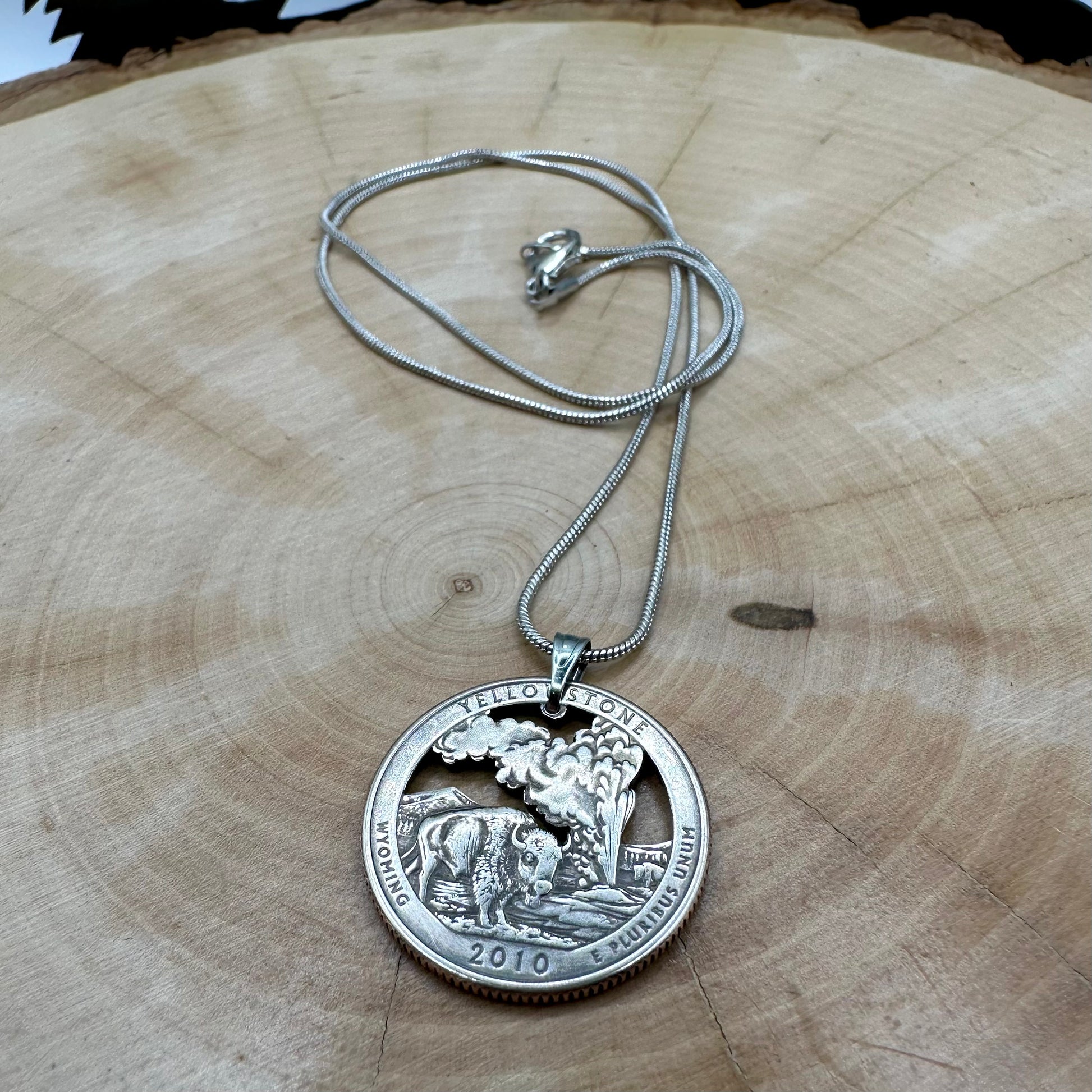 U.S. Yellowstone National Park Quarter Hand Cut Coin Necklace with snake chain on a light wood background. - Mountainstruck Coin Jewelry