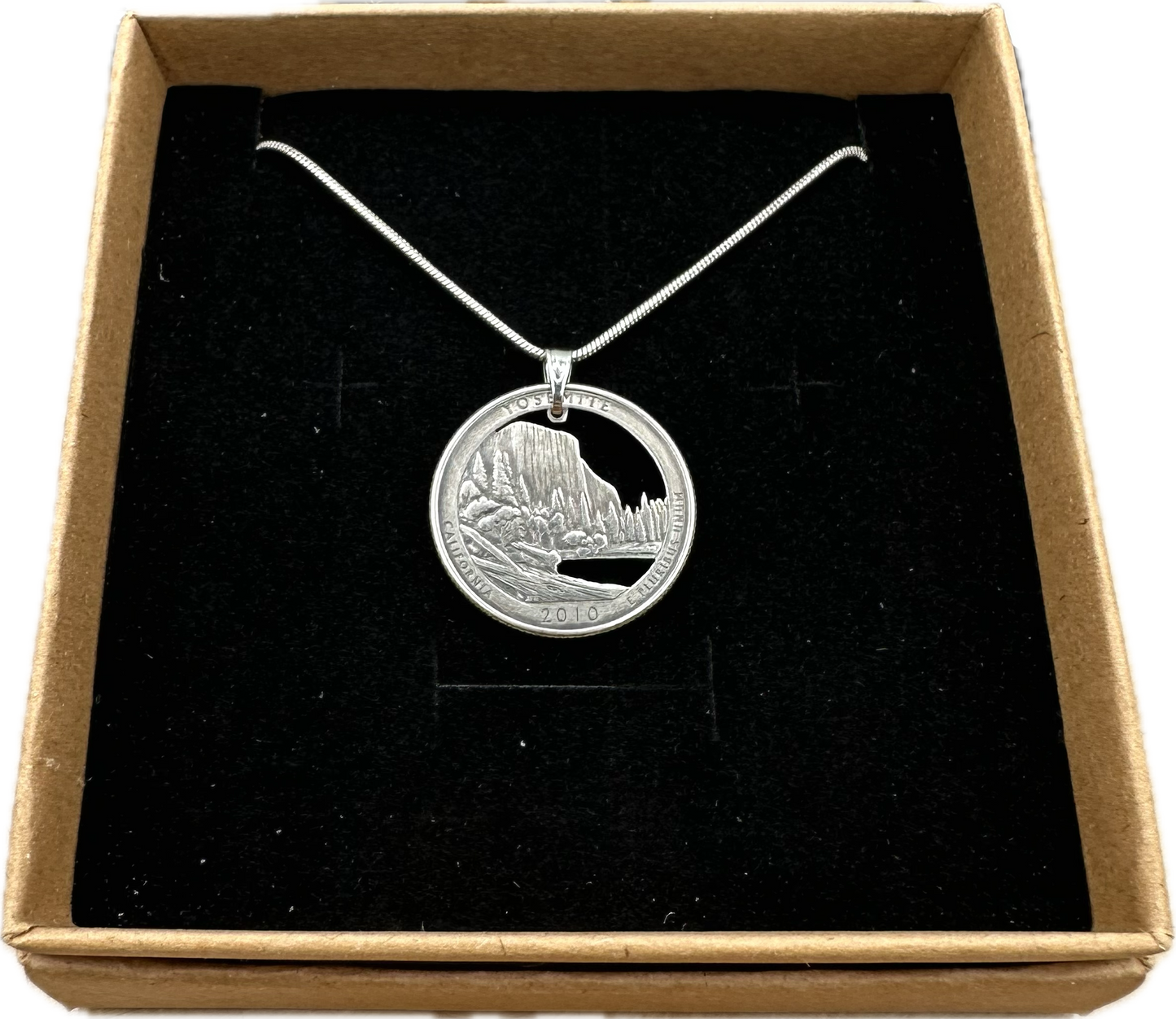 U.S. Yosemite National Park Quarter Hand Cut Coin Necklace with snake chain in a brown kraft box on a black velvet background. - Mountainstruck Coin Jewelry