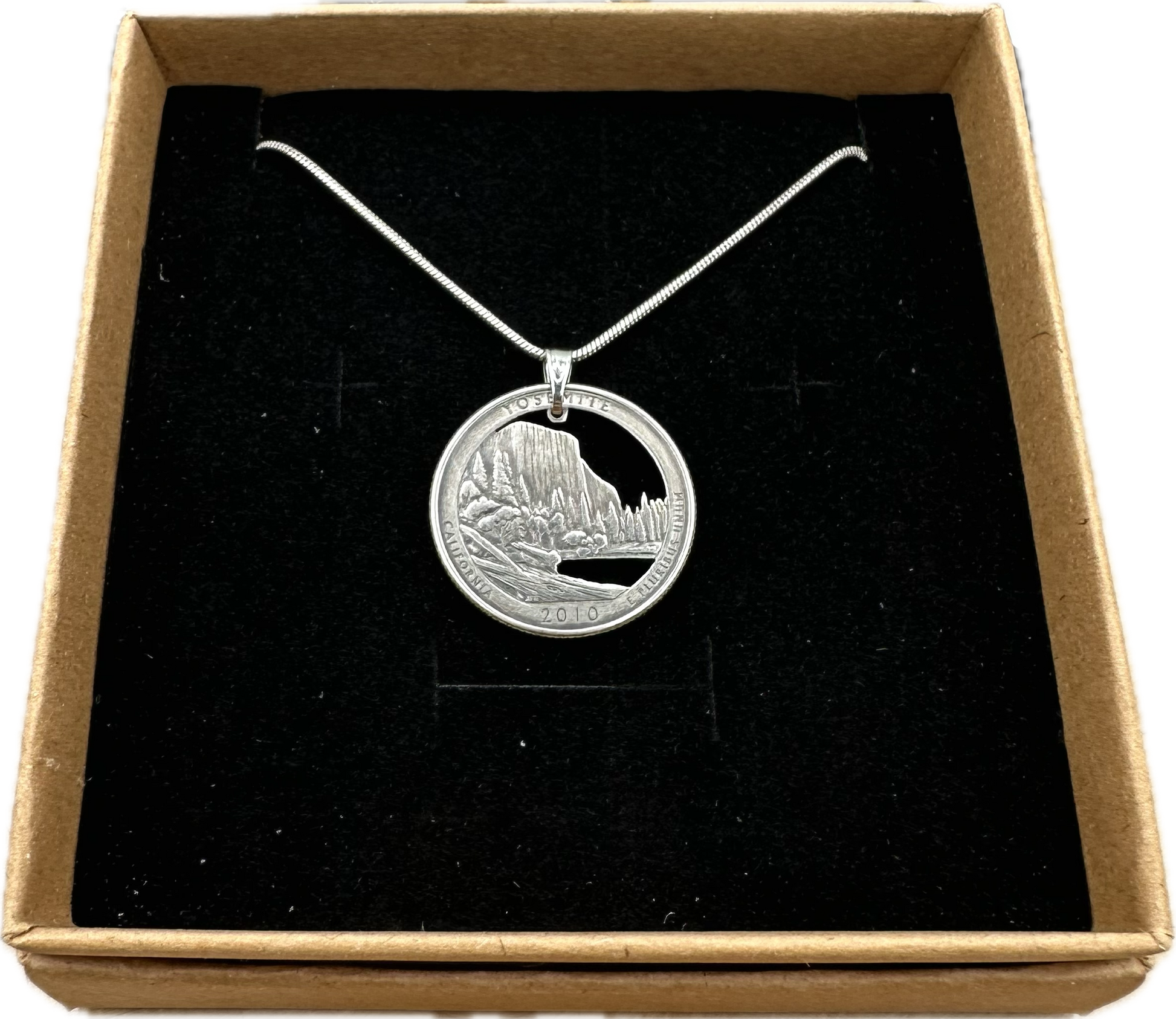 U.S. Yosemite National Park Quarter Hand Cut Coin Necklace with snake chain in a brown kraft box on a black velvet background. - Mountainstruck Coin Jewelry