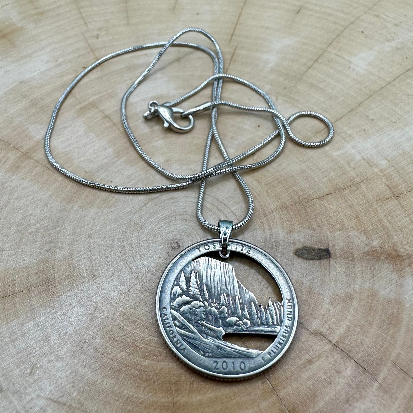 U.S. Yosemite National Park Quarter Hand Cut Coin Necklace with snake chain on a light wood round. - Mountainstruck Coin Jewelry