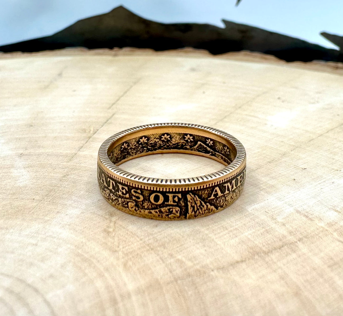 22k U.S. Gold Half Eagle $5 Coin Ring in a light wood round with metal mountains in the background. - Mountainstruck Coin Jewelry