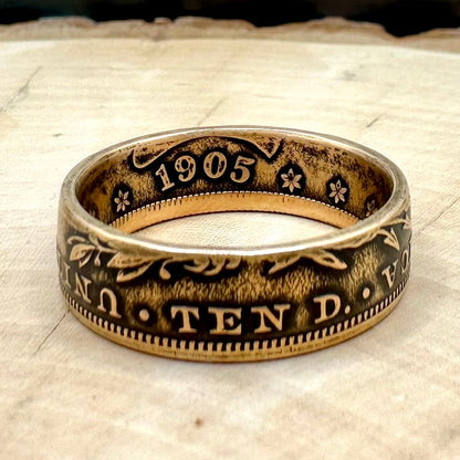 22k U.S. Gold Eagle $10 Coin Ring on a light wood round with a metal mountain background. - Mountainstruck Coin Jewelry