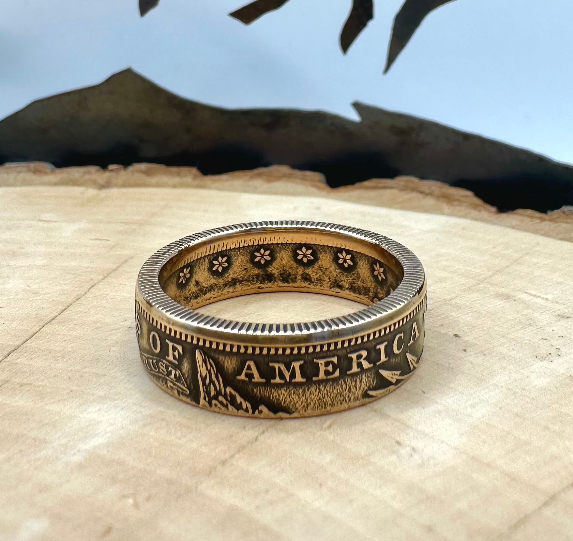 22k U.S. Gold Eagle $10 Coin Ring on a light wood round with a metal mountain background. - Mountainstruck Coin Jewelry