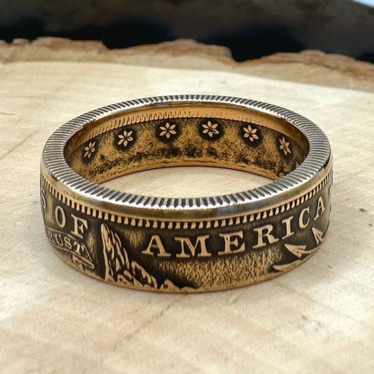 22k U.S. Gold Eagle $10 Coin Ring on a light wood round with a metal mountain background. - Mountainstruck Coin Jewelry