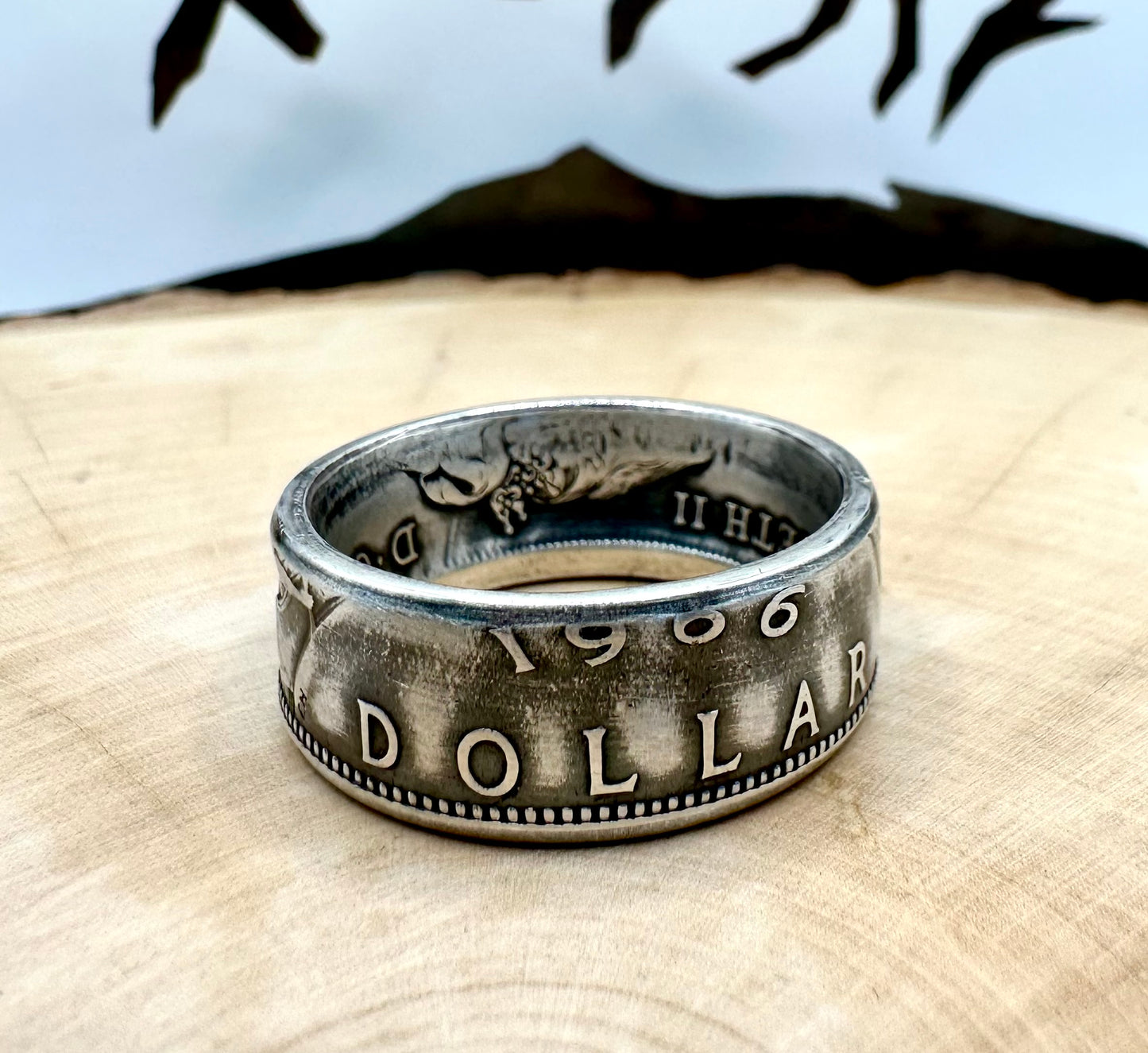 Canada Dollar Silver Coin Ring on a light wood round with a metal mountain background. - Mountainstruck Coin Jewelry