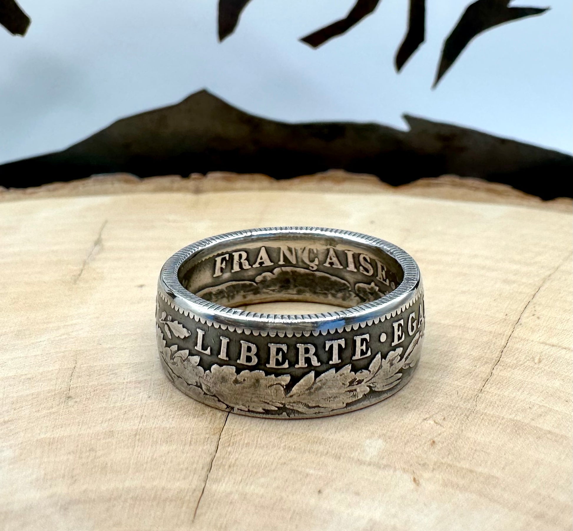 France 2 Franc Silver Coin Ring on a light wood round with a metal mountain background. - Mountainstruck Coin Jewelry