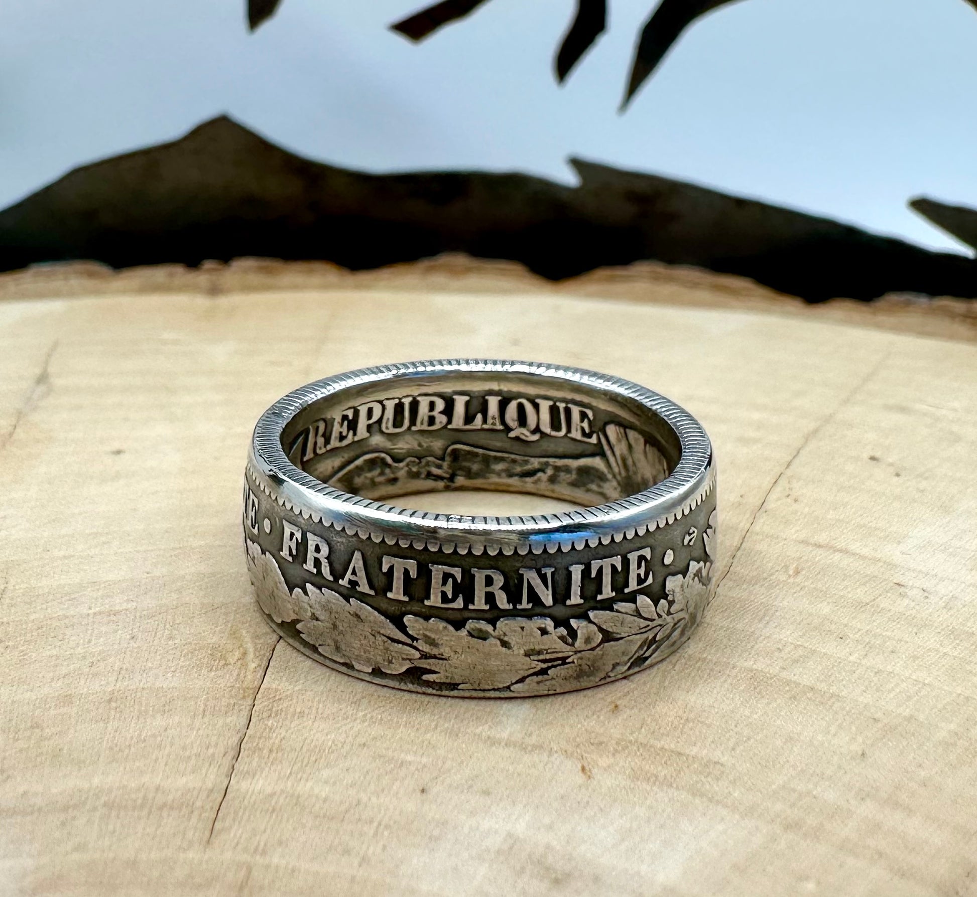 France 2 Franc Silver Coin Ring on a light wood round with a metal mountain background. - Mountainstruck Coin Jewelry