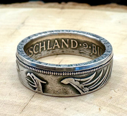 German Eagle 5 Mark Silver Coin Ring on light wood round with a metal mountain background. - Mountainstruck Coin Jewelry
