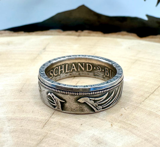 German Eagle 5 Mark Silver Coin Ring on light wood round with a metal mountain background. - Mountainstruck Coin Jewelry