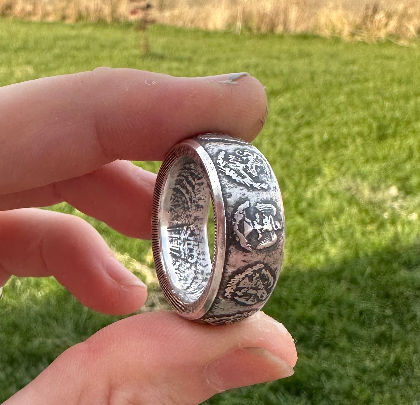 Mexico 1oz Libertad .999 Silver Coin Ring held on its side in front green grass. - Mountainstruck Coin Jewelry