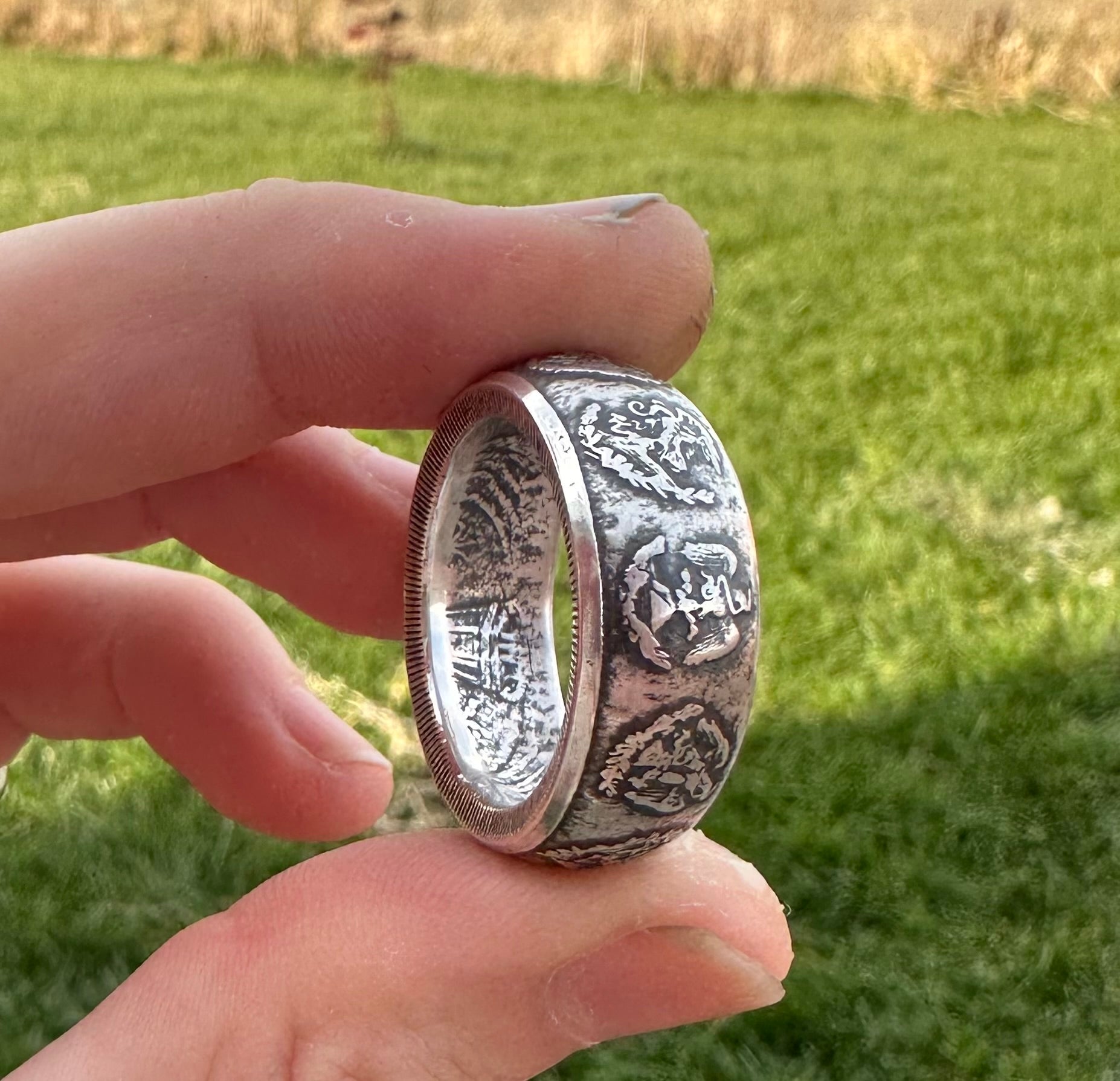 Mexico 1oz Libertad .999 Silver Coin Ring held on its side in front green grass. - Mountainstruck Coin Jewelry
