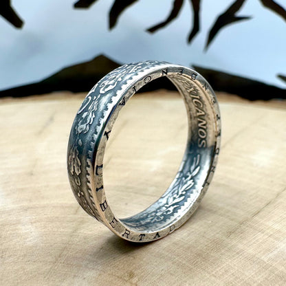 Mexico 50 Centavos Silver Coin Ring (Rare) on its edge on a light wood round with mountain outline in the background. 
- Mountainstruck Coin Jewelry
