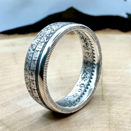 Mexico Aztec Calendar 1/4 oz Silver Round Ring on edge on a light wood round with a metal mountain background. 
- Mountainstruck Coin Jewelry
