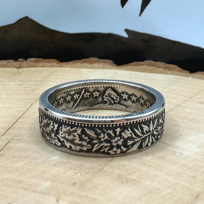 Swiss 2 Franc Silver Coin Ring (patina) on a light wood round with mountain outline in the background. - Mountainstruck Coin Jewelry