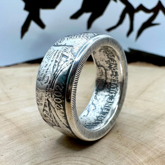 U.S. 1oz 999 Silver Eagle $1 Coin Ring on its side on a light wood round with a metal mountain background. - Mountainstruck Coin Jewelry