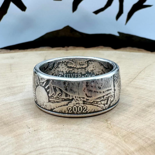 U.S. 1oz 999 Silver Eagle $1 Coin Ring on a light wood round with a metal mountain background. - Mountainstruck Coin Jewelry