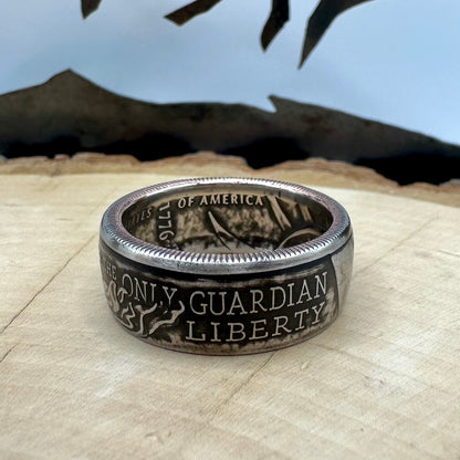 U.S. 2026 Half Dollar Coin Ring on a light wood round with a metal mountain background. - Mountainstruck Coin Jewelry
