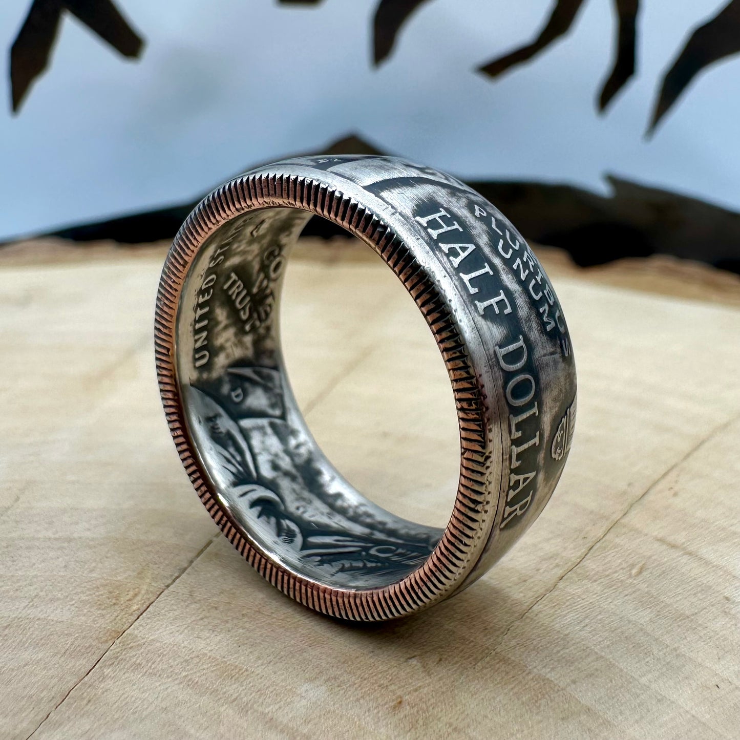 U.S. 2026 Half Dollar Coin Ring on its edge on a light wood round with a metal mountain background. - Mountainstruck Coin Jewelry