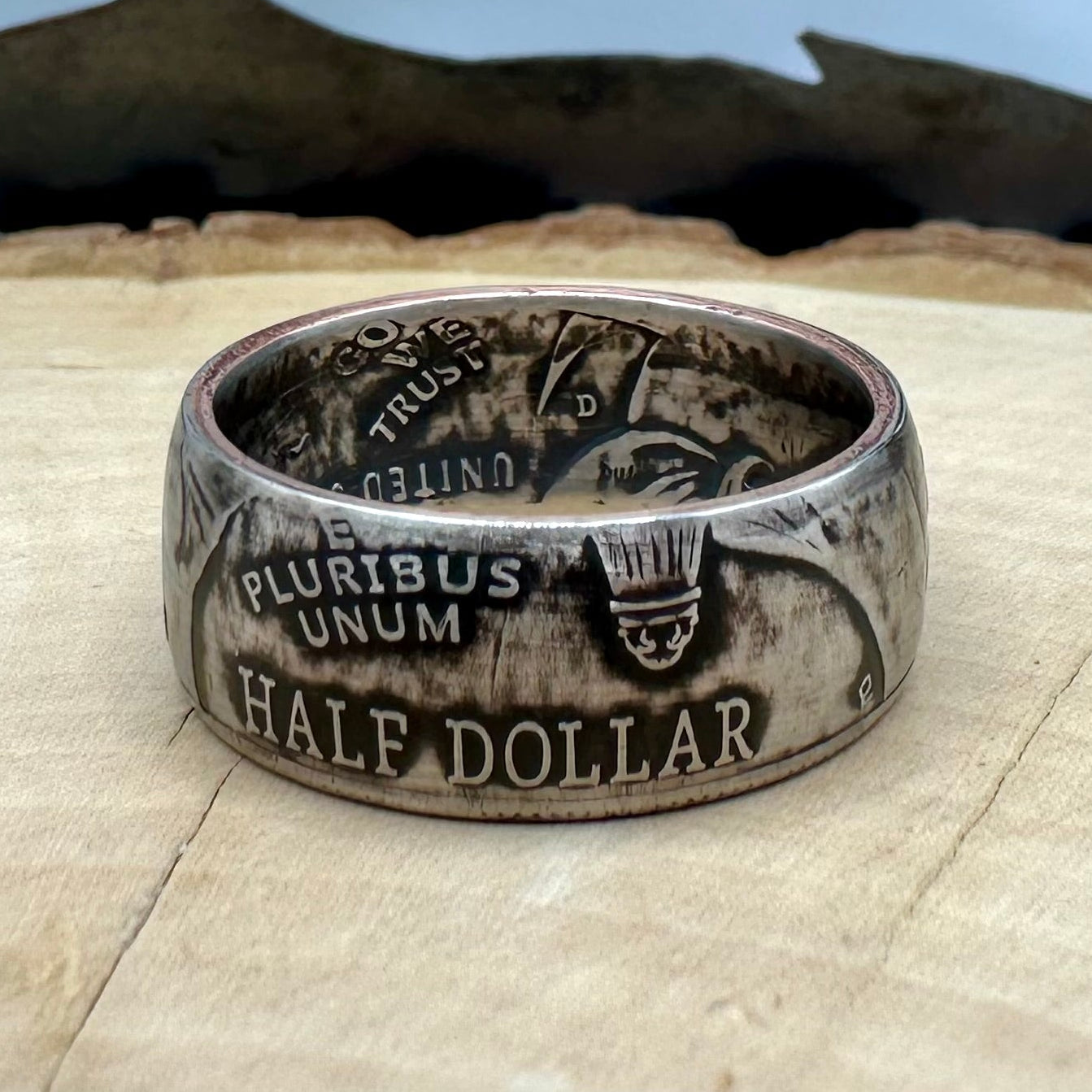 U.S. 2026 Half Dollar Coin Ring on a light wood round with a metal mountain background. - Mountainstruck Coin Jewelry
