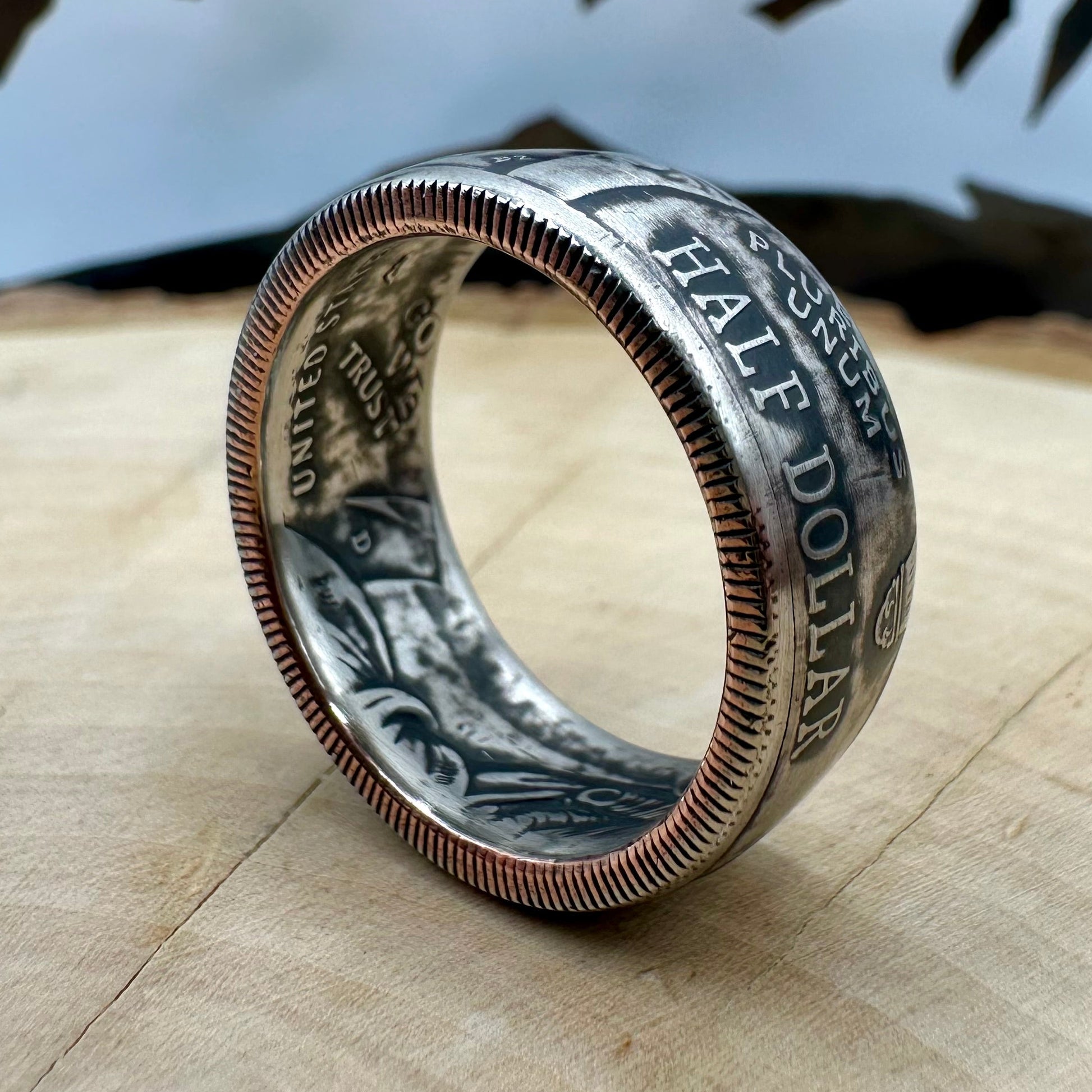 U.S. 2026 Half Dollar Coin Ring on its edge on a light wood round with a metal mountain background. - Mountainstruck Coin Jewelry