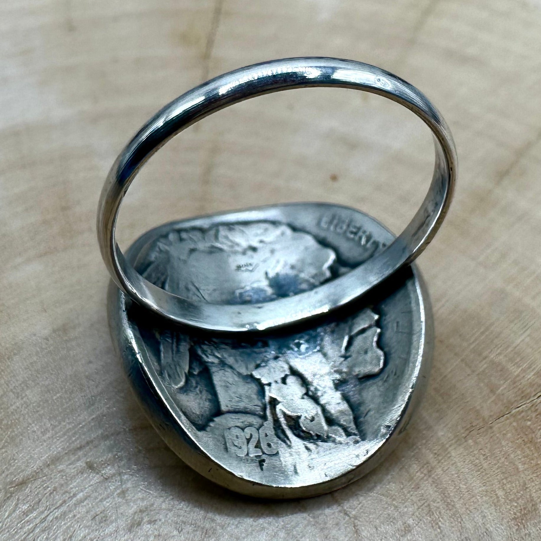 U.S. Buffalo Nickel Coin Signet Ring (Buffalo Side) with a sterling silver band on a light wood round with a metal mountain background. - Mountainstruck Coin Jewelry
