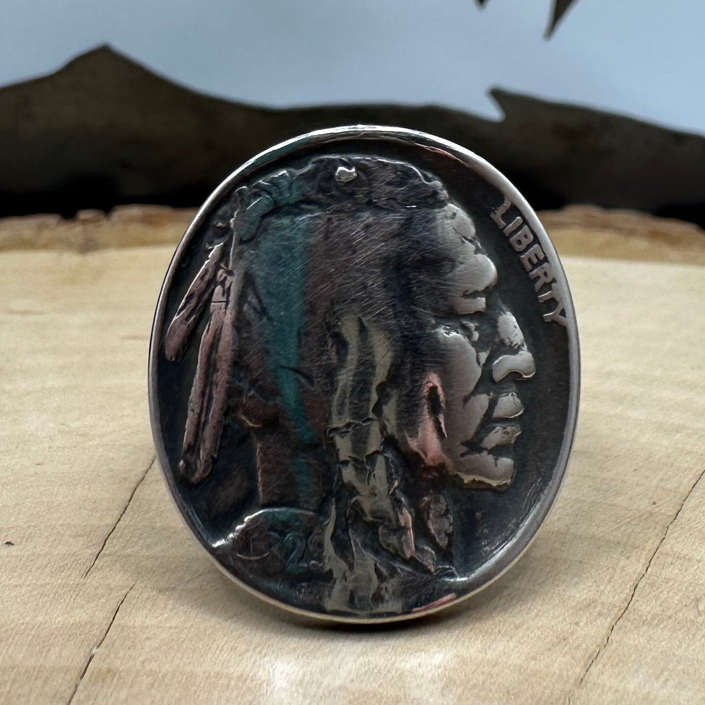 U.S. Buffalo Nickel Coin Signet Ring (Native side) with a sterling silver band on a light wood round with a metal mountain background. - Mountainstruck Coin Jewelry