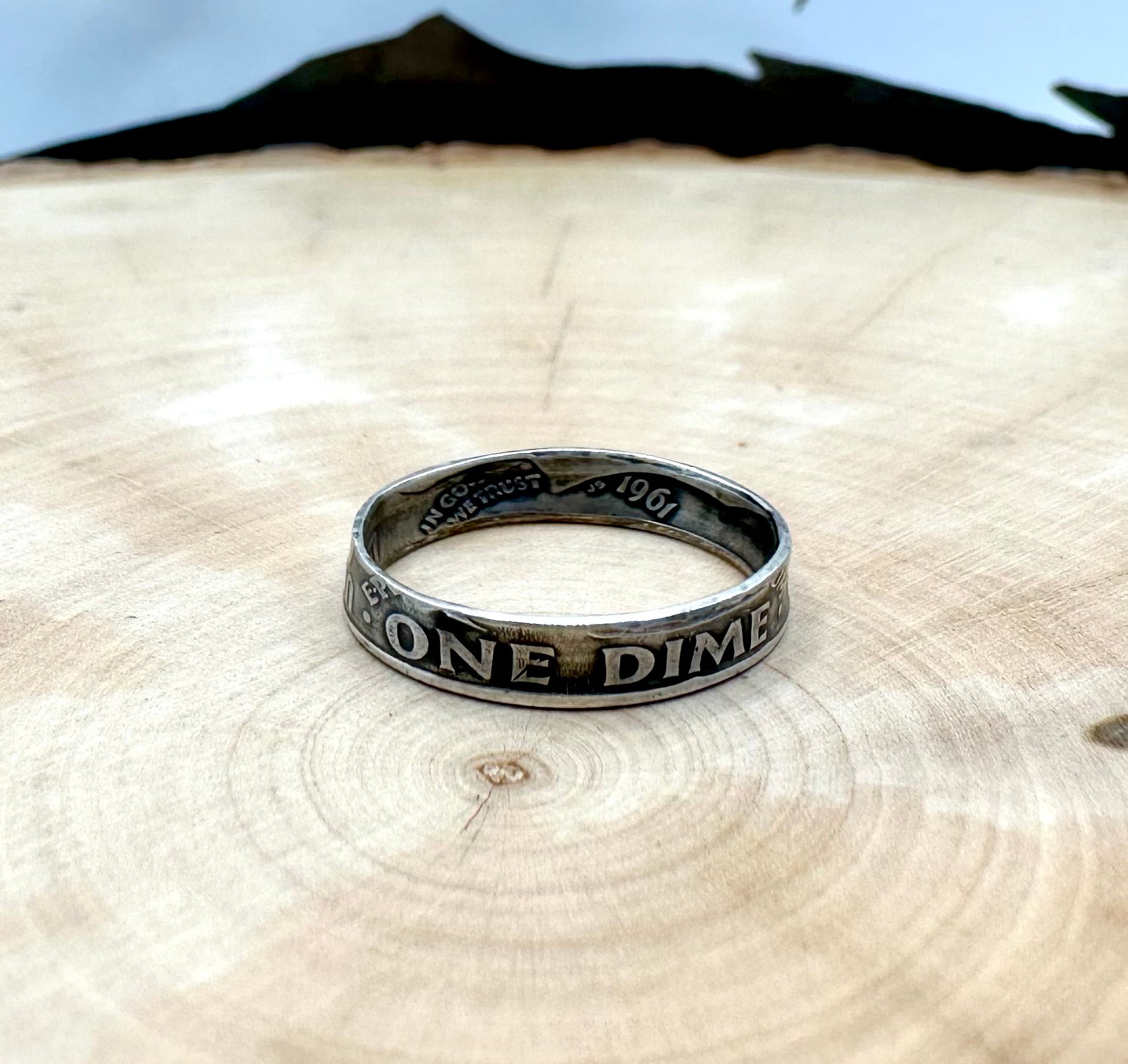 U.S. Dime Silver Coin Ring patina on a light wood round with a metal mountain background. - Mountainstruck Coin Jewelry