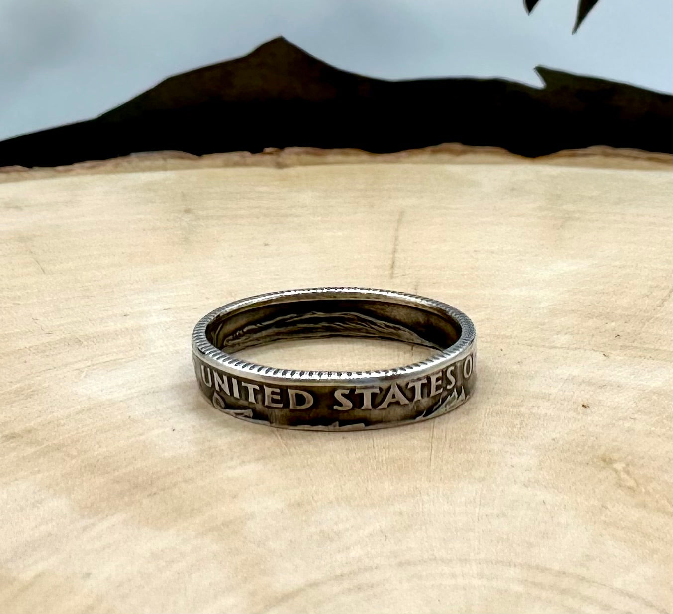 U.S. Dime Silver Coin Ring patina on a light wood round with a metal mountain background. - Mountainstruck Coin Jewelry