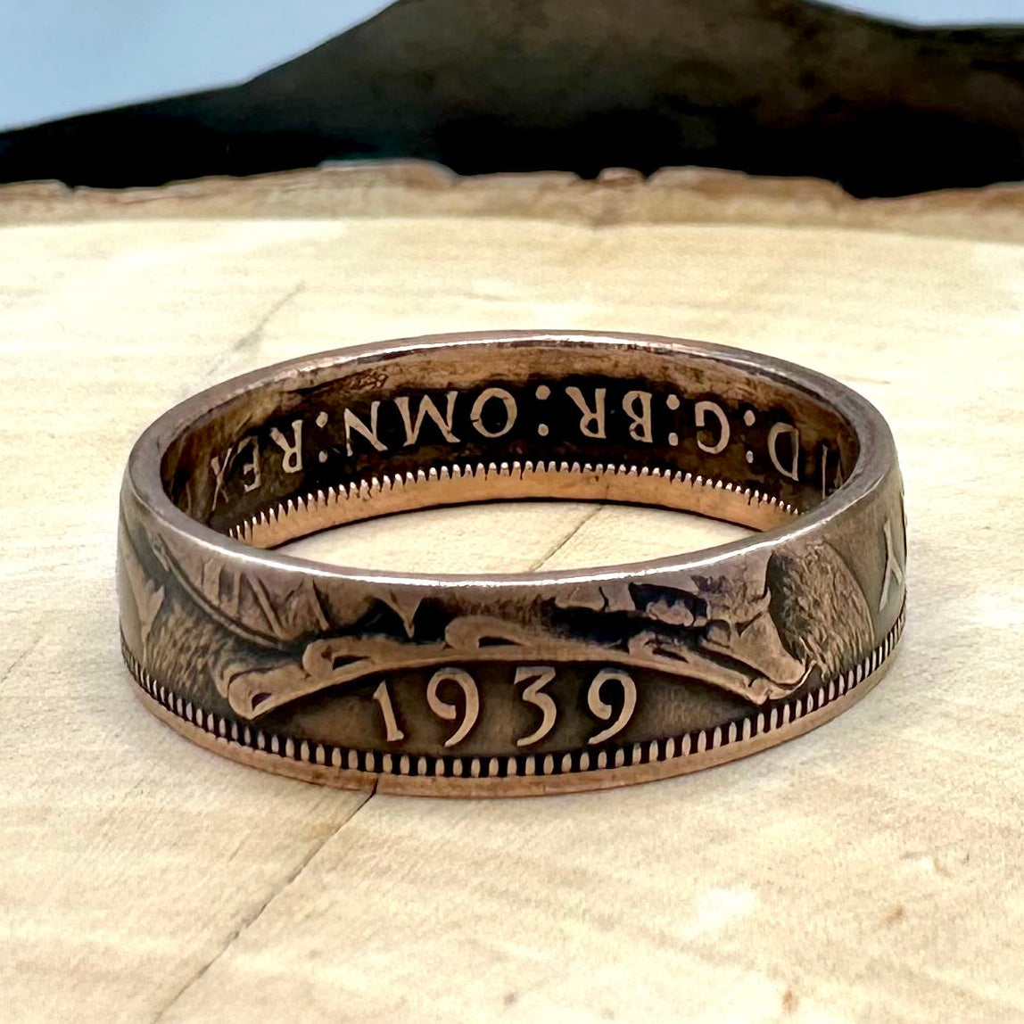 UK One Penny Coin Ring on a light wood round with metal mountain background. - Mountainstruck Coin Jewelry
