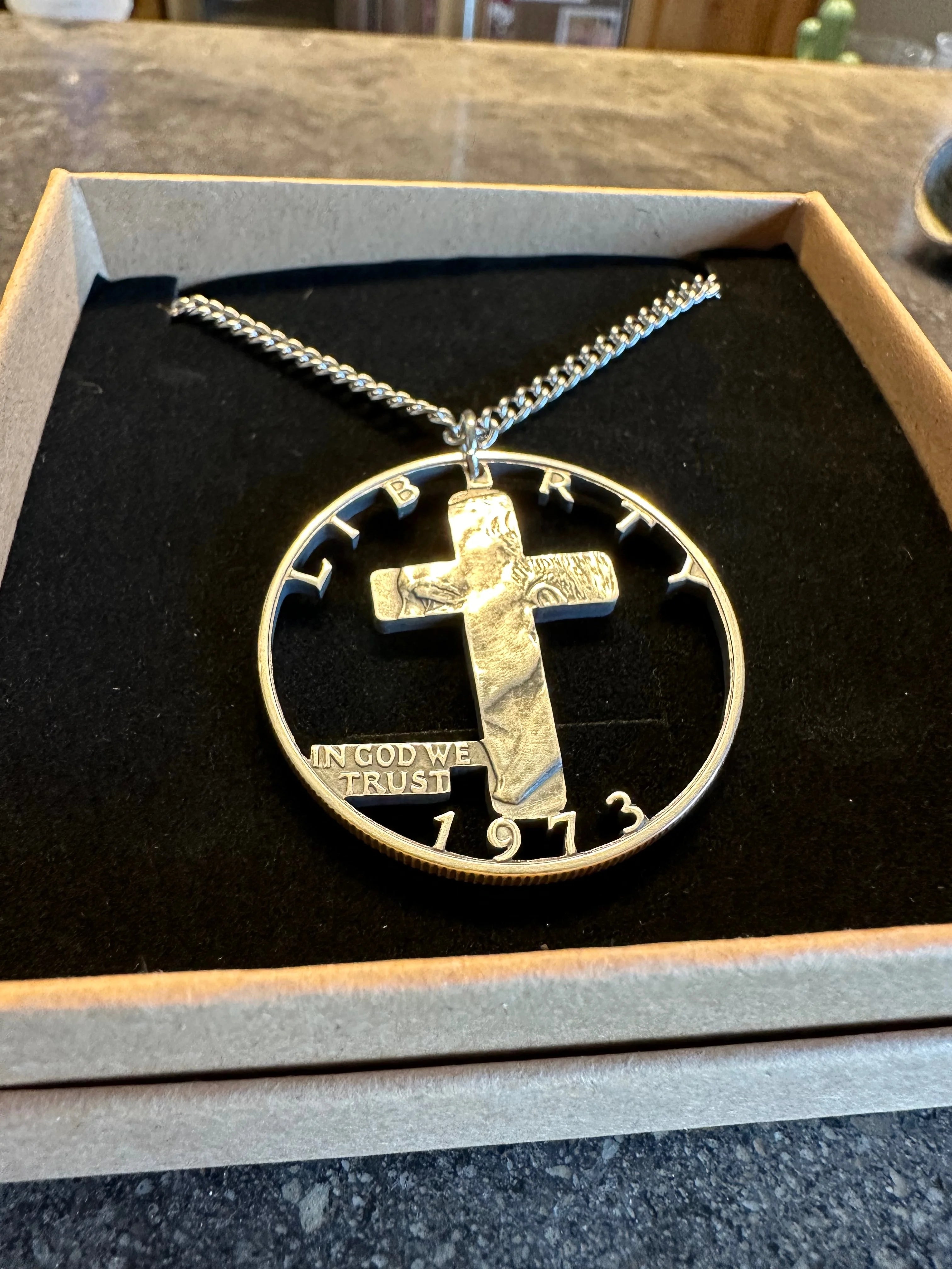 Silver Half Dollar coin necklace with a cross hand cut out on a black cushion in a box. -Mountainstruck Coin Jewelry
