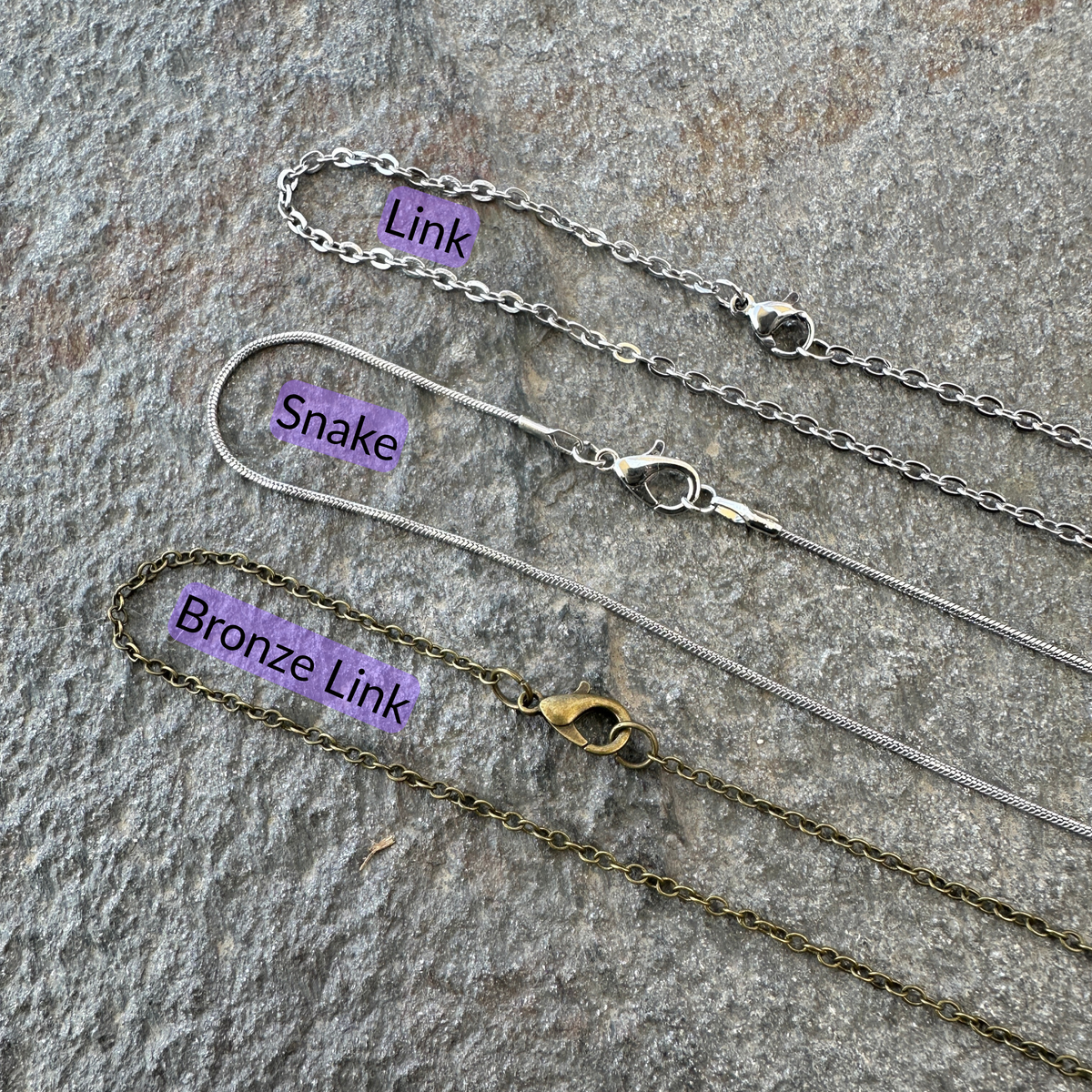 Link chain, snake chain, and bronze link chains set on a gray stone surface with black text and light purple background for each type of chain. 
- Mountainstruck Coin Jewelry