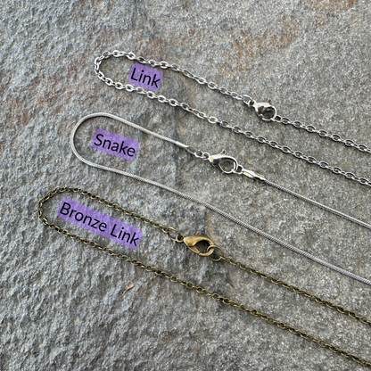 Link chain, snake chain, and bronze link chains set on a gray stone surface with black text and light purple background for each type of chain. 
- Mountainstruck Coin Jewelry