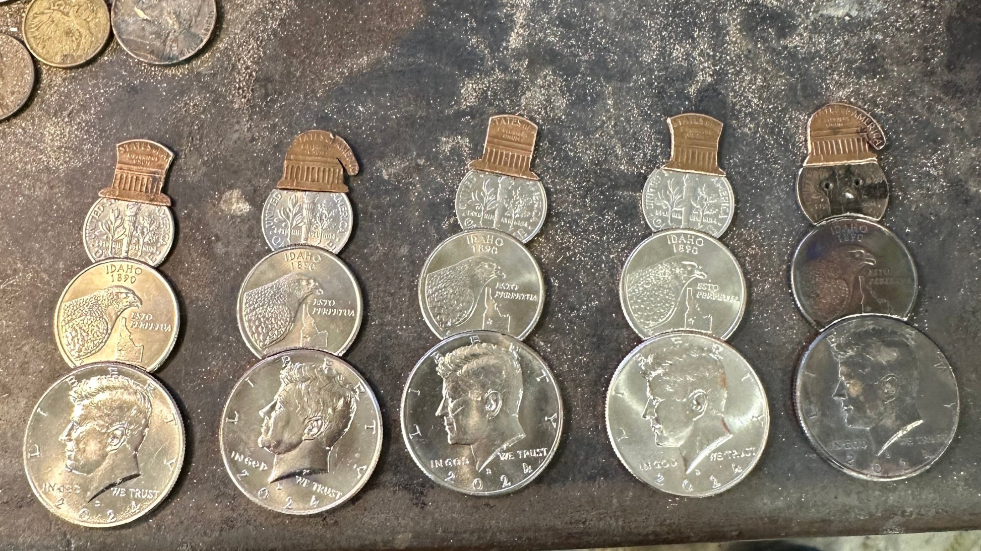 2024 Snowman Coin Christmas Ornament with a selection of U.S. coins (penny, dime, Idaho Quarter, and 2024 uncirculated half dollar) soldered into a snowman with a red ribbon scarf and golden tassel  on a metal background. - Mountainstruck Coin Jewelry