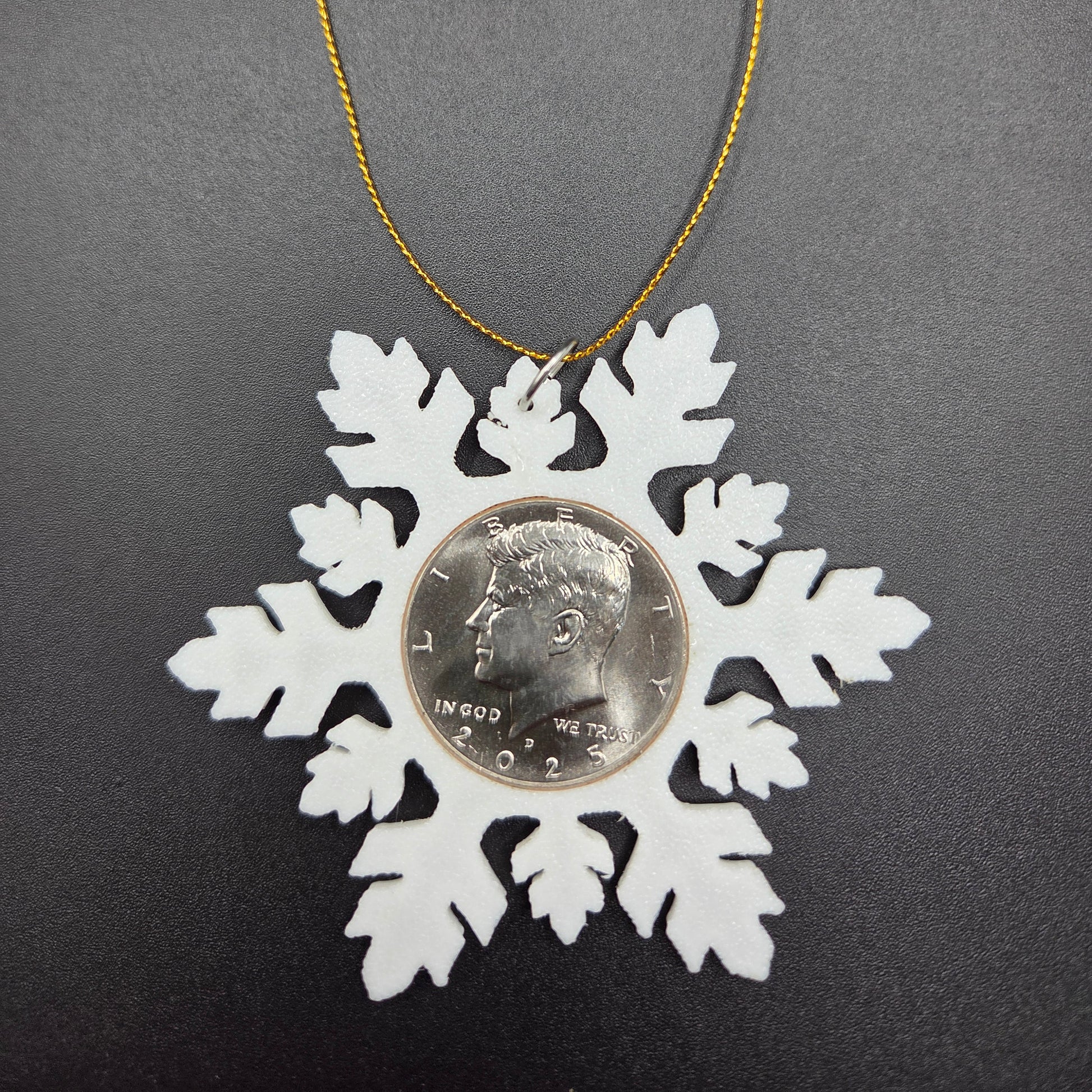 2025 Half Dollar Christmas Ornament  with an uncirculated half dollar cased inside a white 3D printed snowflake with golden tassel on a black background. - Mountainstruck Coin Jewelry