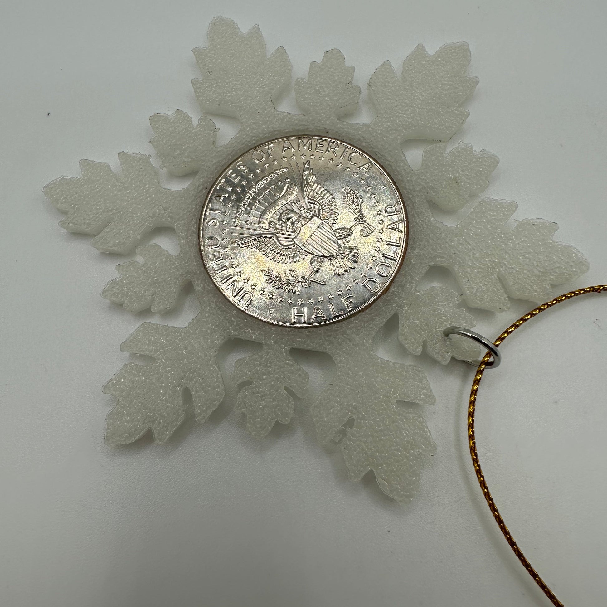 2025 Half Dollar Christmas Ornament (glows) back with an uncirculated half dollar cased inside a white 3D printed snowflake with golden tassel on a white background. - Mountainstruck Coin Jewelry
