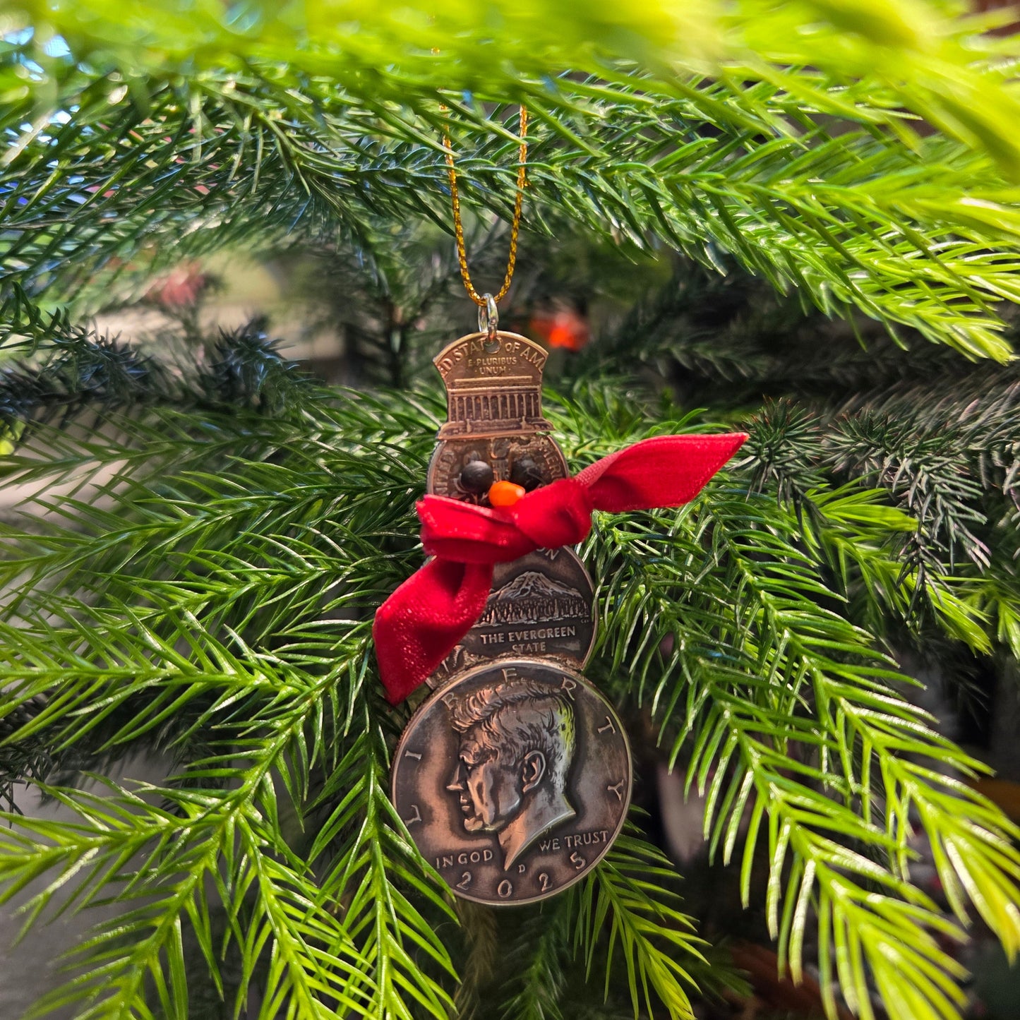 2025 Snowman Coin Christmas Ornament with a selection of U.S. coins (penny, dime, state quarter, and 2025 uncirculated half dollar) soldered into a snowman with a red ribbon scarf and golden tassel in front of a green pine tree. - Mountainstruck Coin Jewelry