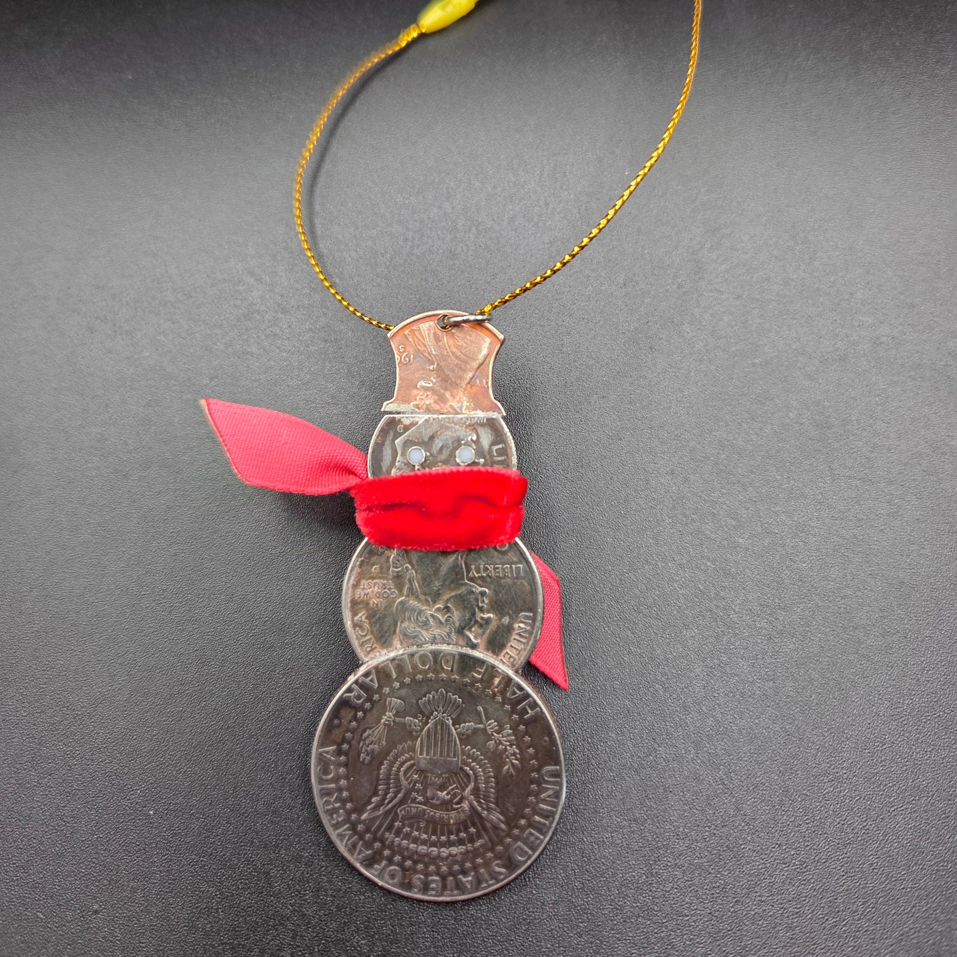 2025 Snowman Coin Christmas Ornament with a selection of U.S. coins (penny, dime, state quarter, and 2025 uncirculated half dollar) soldered into a snowman with a red ribbon scarf and golden tassel on a black background. - Mountainstruck Coin Jewelry