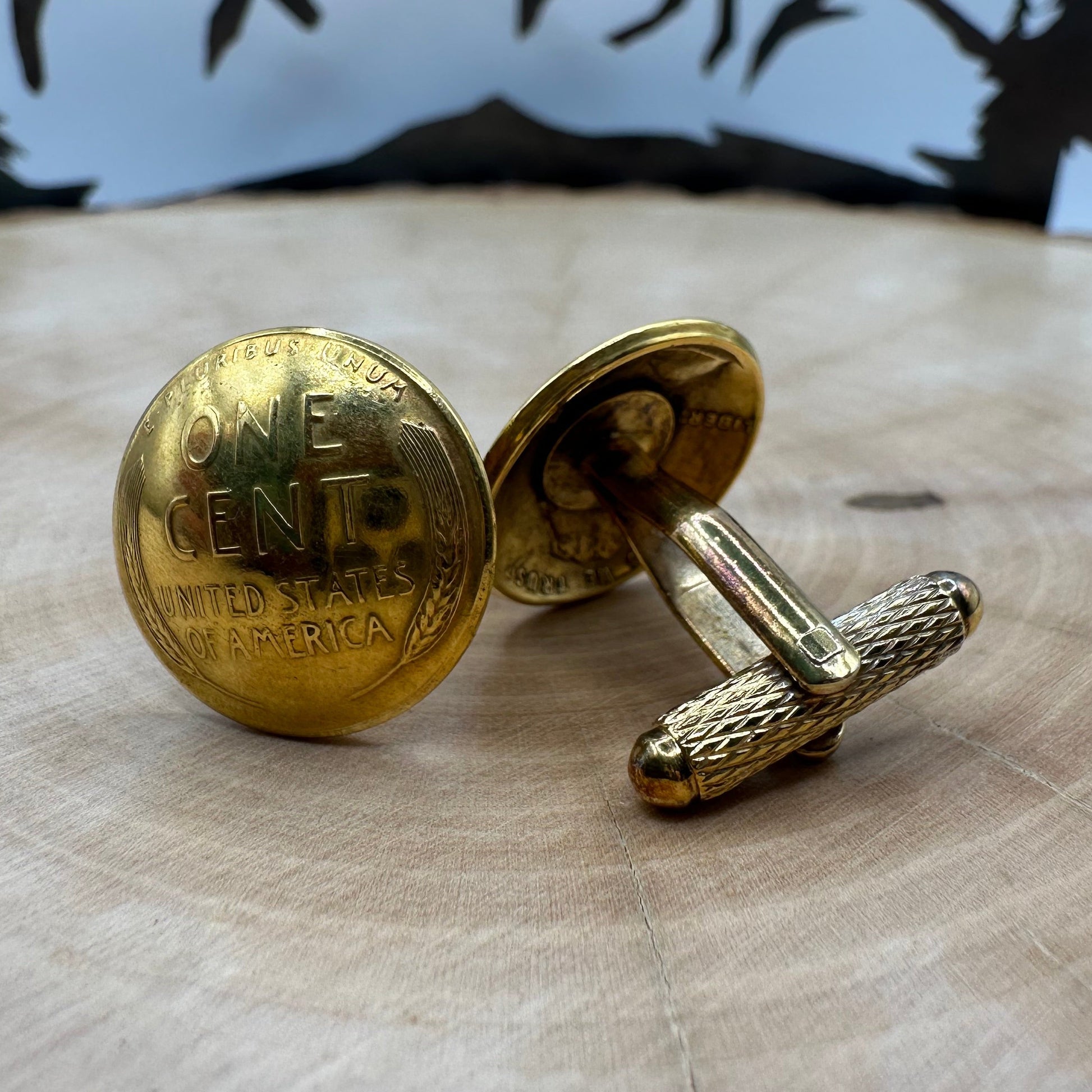 24k Gold Plate U.S. Wheat Penny Coin Cufflinks on a light wood round with a metal mountain background. - Mountainstruck Coin Jewelry