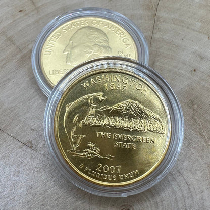 U.S. Washington Quarter 24k Gold Plated Coin in a plastic case on a light wood round on top of the back of a U.S. Washington Quarter 24k Gold Plated Coin in a plastic case.
- Mountainstruck Coin Jewelry