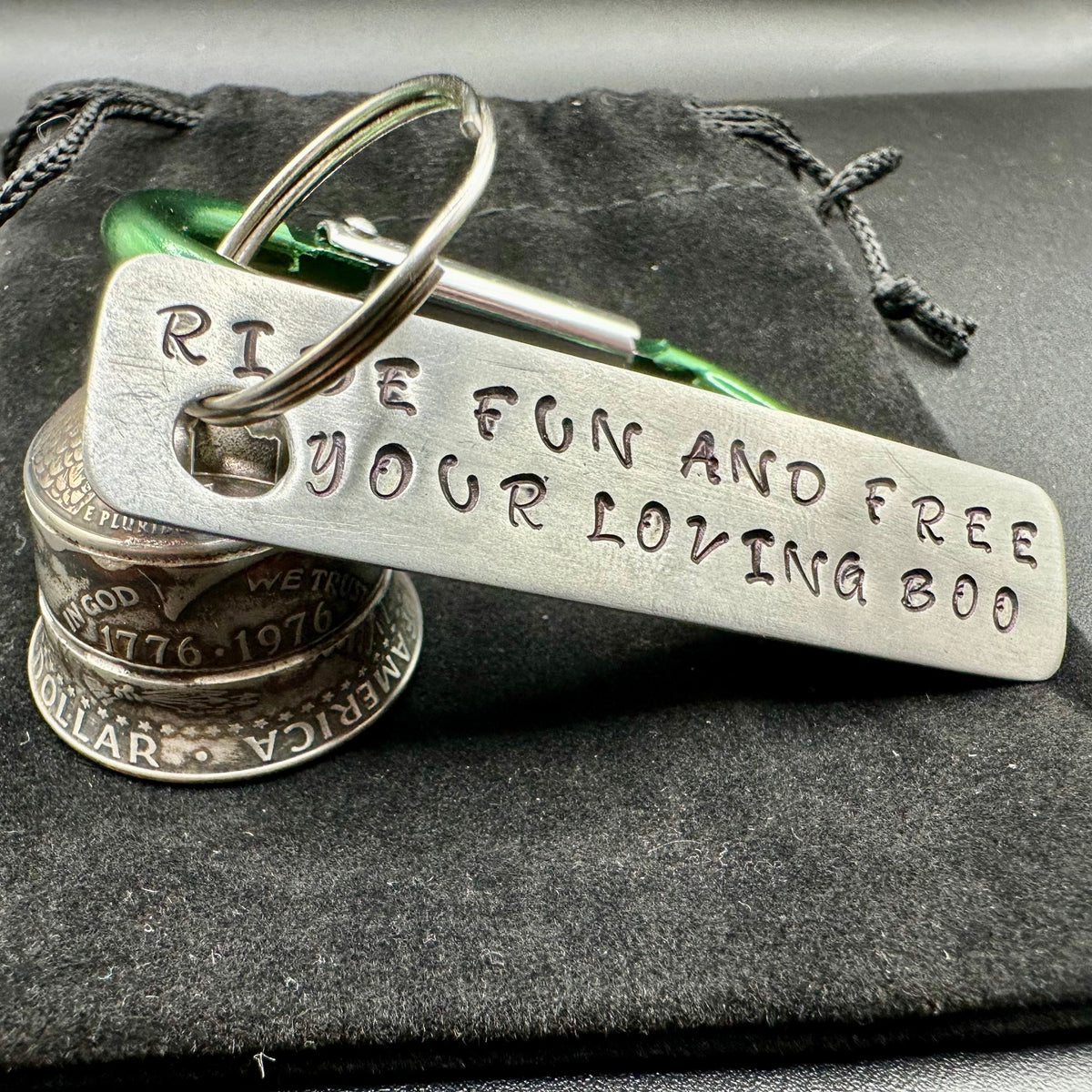 Green keychain with engraved text "ride fun and free your loving boo" on a metal surface with a gremlin bell made of coins. 
- Mountainstruck Coin Jewelry